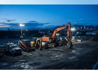 Commercial excavator and equipment fleet staged on a construction yard at blue-hour dawn