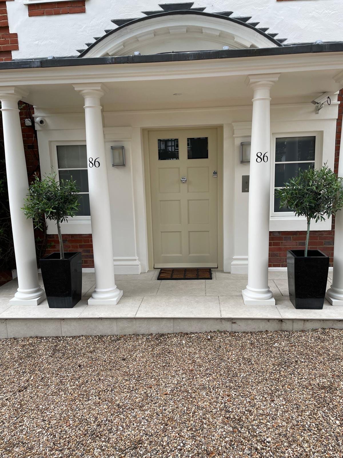 Portico entrance with panelled front door, white columns and olive planters