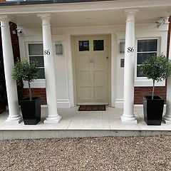 Portico entrance with panelled front door, white columns and olive planters