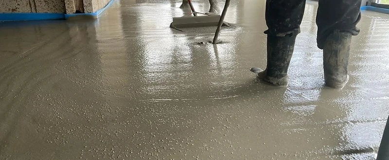 Workers spreading and levelling wet floor screed on site — MPC Plastering
