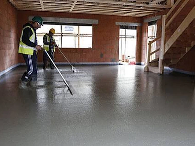Two workers levelling wet floor screed with long-handled tools — MPC Plastering