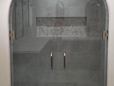 Arched glass shower enclosure with herringbone surround and dual doors
