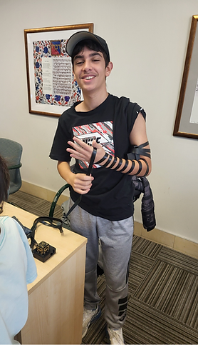 A BMC boy smiling as he learns to wrap tefillin during a session