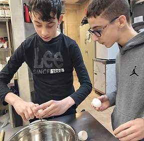 Two boys cracking eggs together during a BMC kitchen session