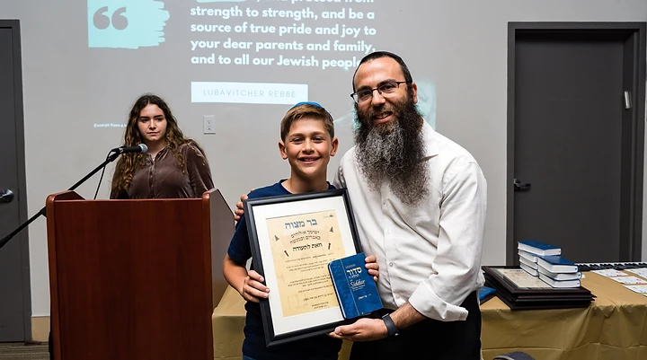 Rabbi Benny presenting a graduate with his Bar Mitzvah certificate and Siddur