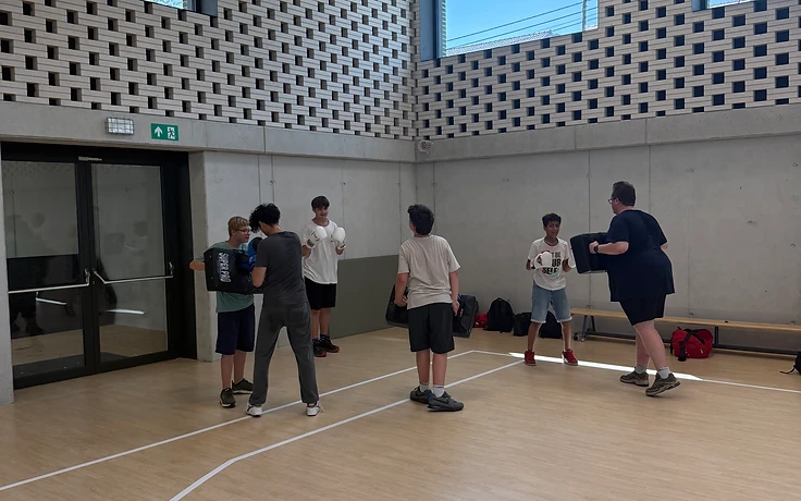 Leerlingen oefenen kickboksdrills met strike shields in een sporthal