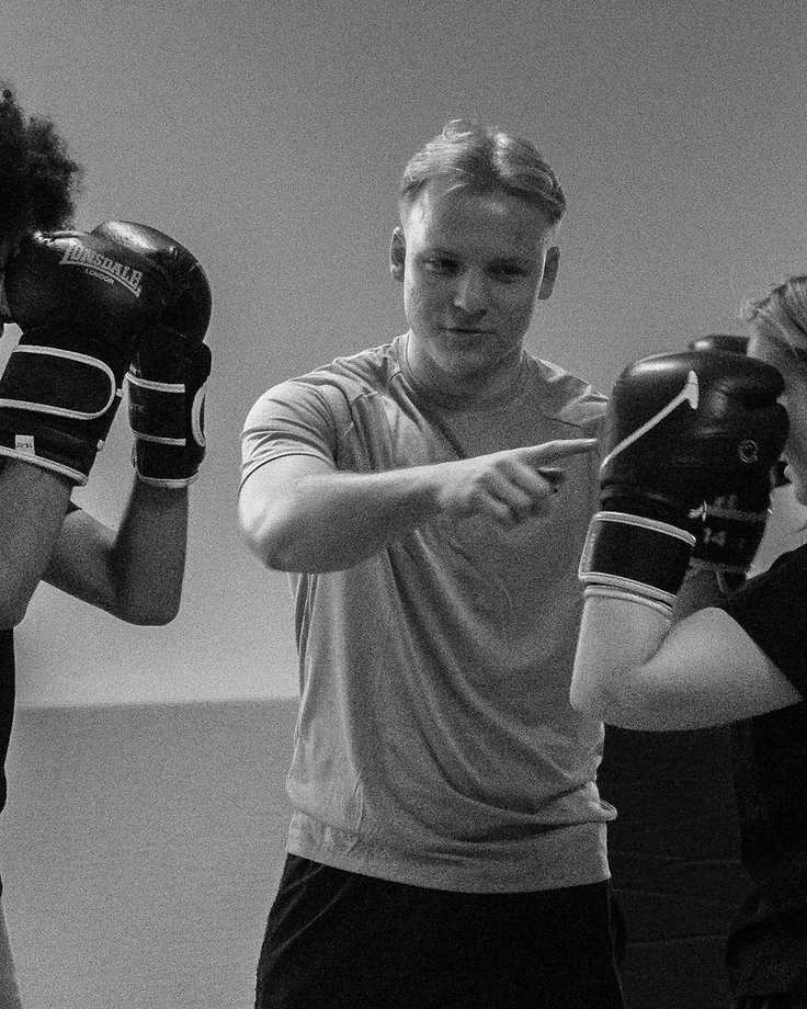 Een trainer begeleidt twee leerlingen tijdens een kickboxsessie