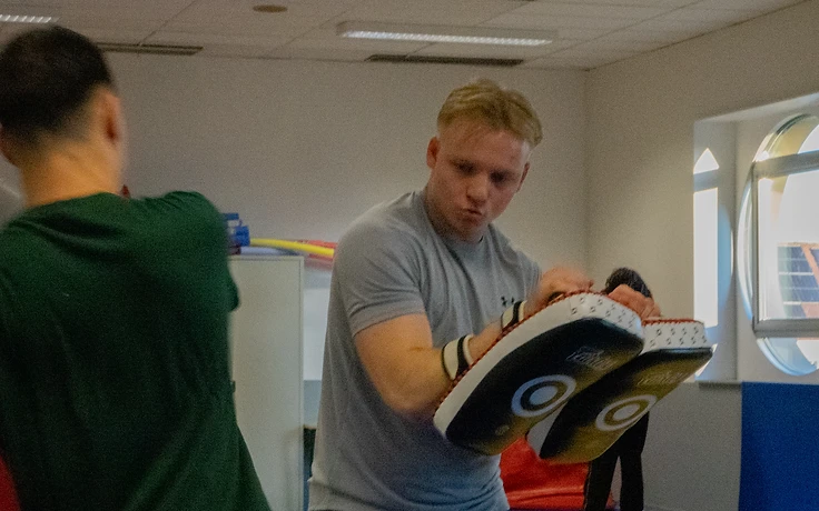 Trainer en leerling in pad work in een gym met een boograam