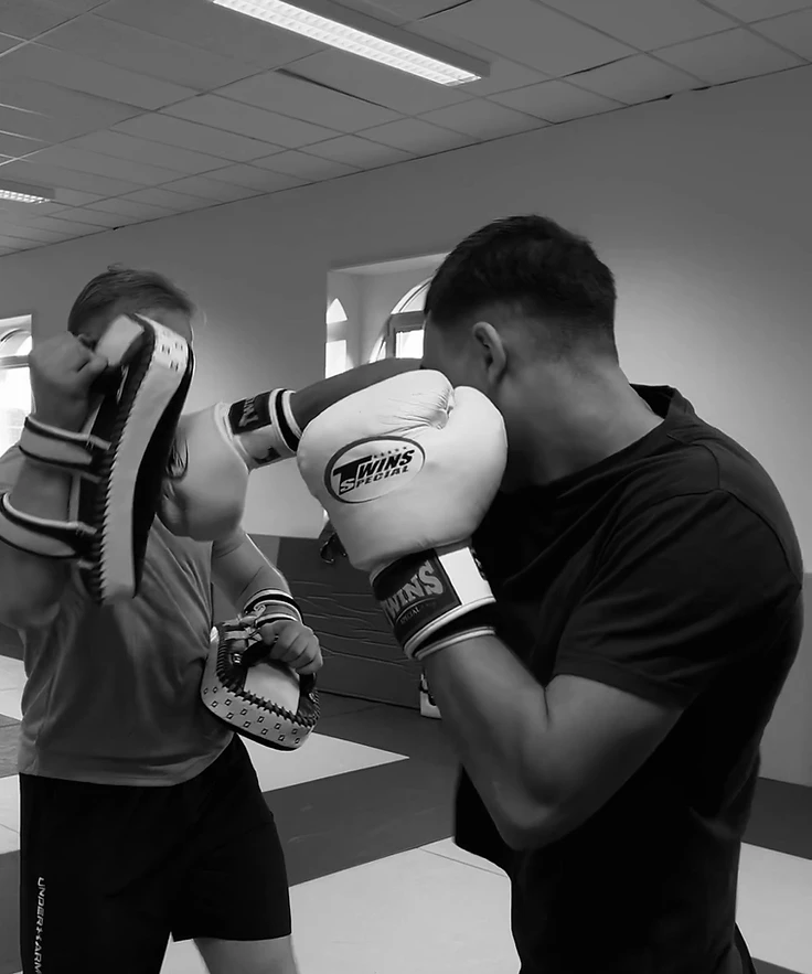 Kickbokstraining: een leerling stompt met bokshandschoenen op de pads van de trainer