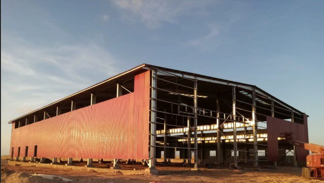 Steel building erection with red siding at golden hour