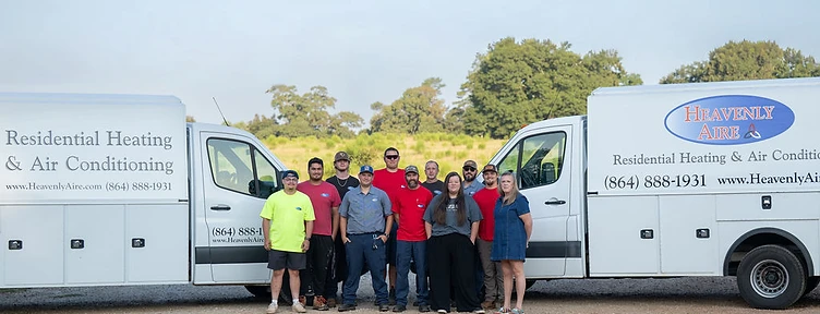 The Heavenly Aire team, including technicians and staff, standing in front of two company service vans in Seneca, SC.