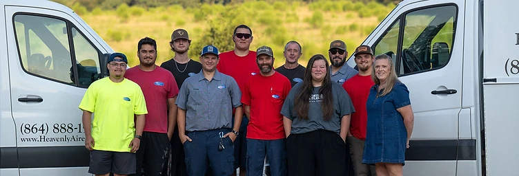 A group portrait of the Heavenly Aire staff standing in front of two company service vans in a gravel parking lot, featuring eleven employees in work attire.