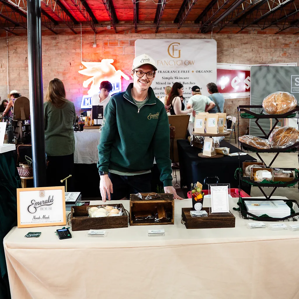 A baker smiling behind the Emerald House booth of fresh sourdough loaves