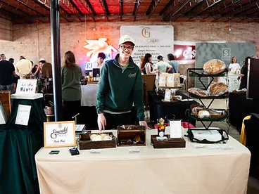 A baker smiling behind the Emerald House booth of fresh sourdough loaves