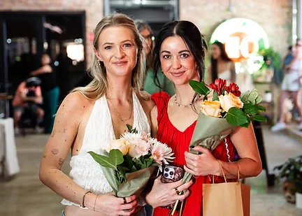 Two friends laughing together with fresh flower bouquets and a shopping tote at the market