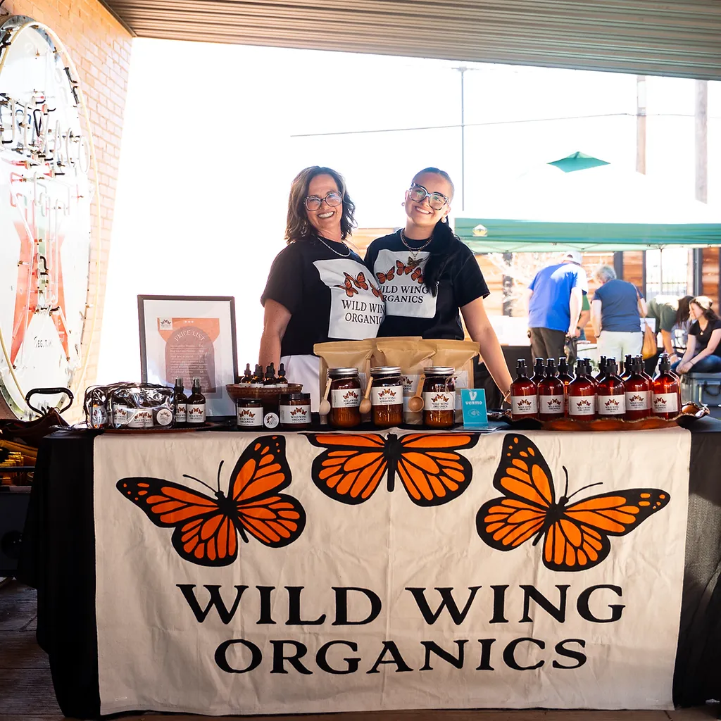 Smiling vendors behind their Wild Wing Organics booth of raw honey jars