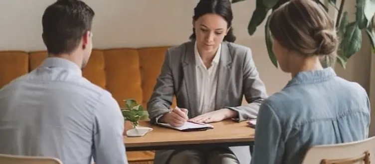 A counselor taking notes across from a couple seated together in a calm, plant-filled office