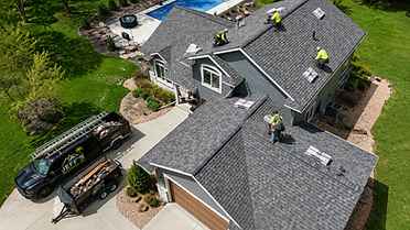 Aerial view of a Jeff's Roofing replacement job with crew on the roof and branded truck and dump trailer in the driveway