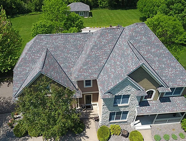 Aerial view of a large multi-story suburban home with a complex asphalt shingle roof