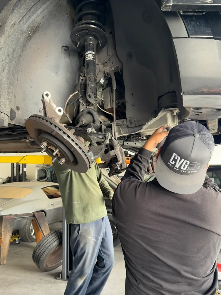 CVG mechanic in a branded cap performing suspension work on a lifted vehicle