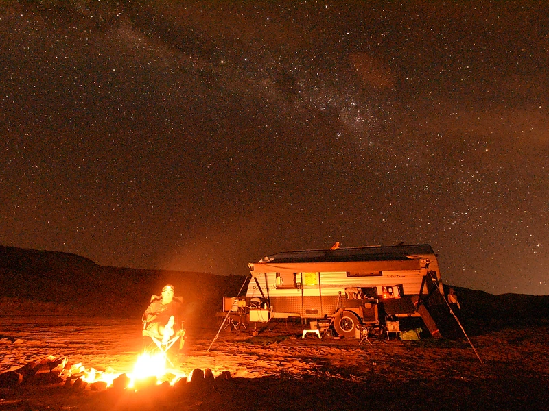 Campfire glowing beside the caravan under a dense field of stars