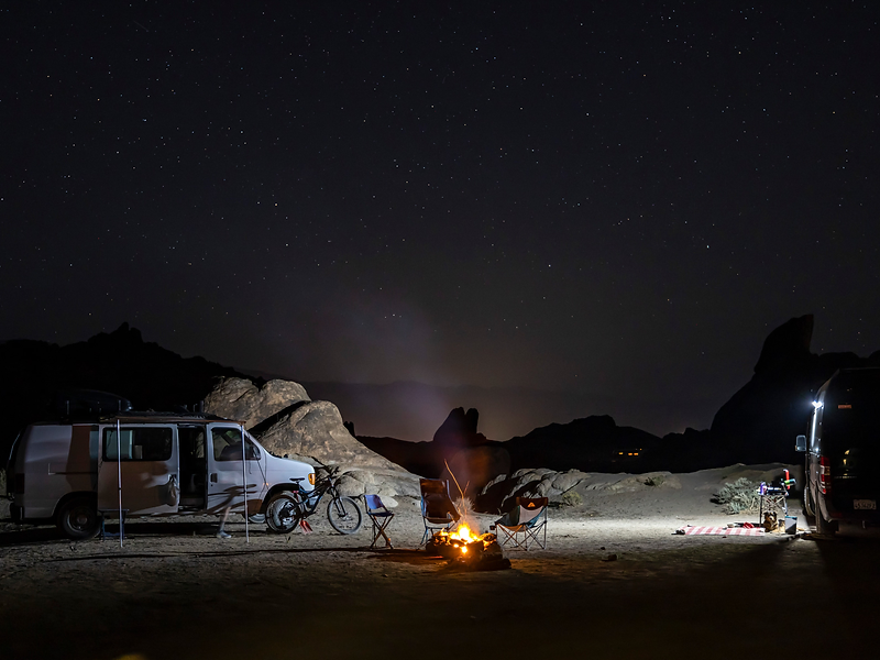 Campfire burning beside a parked van at a remote outback campsite under a starry sky