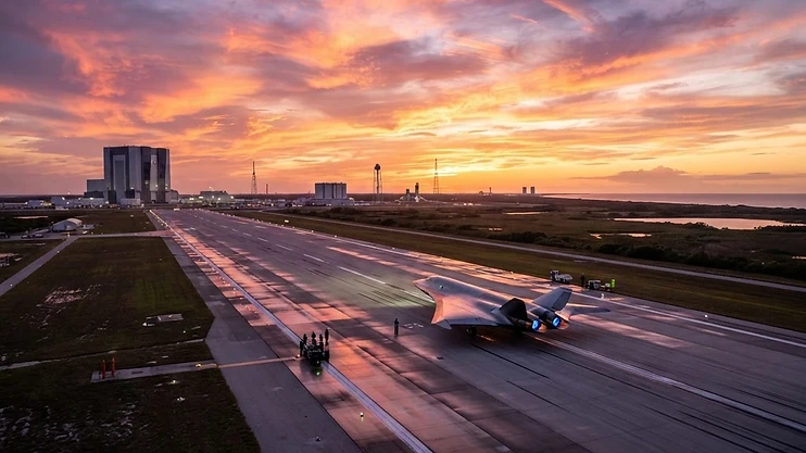 A futuristic aircraft on the runway at the Kennedy Space Center during sunset.
