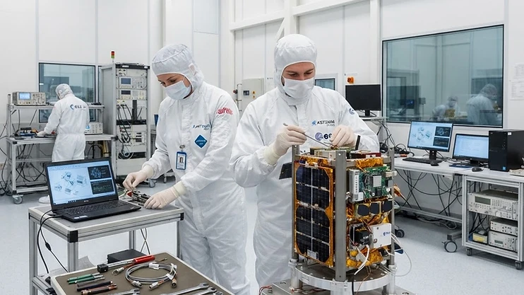 Engineers working on a small satellite in a clean room facility.