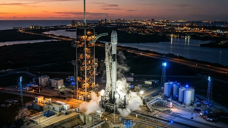 Rocket launch pad at dusk with city lights in the background.