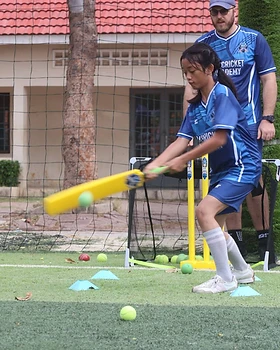 A young player mid-swing with her coach watching
