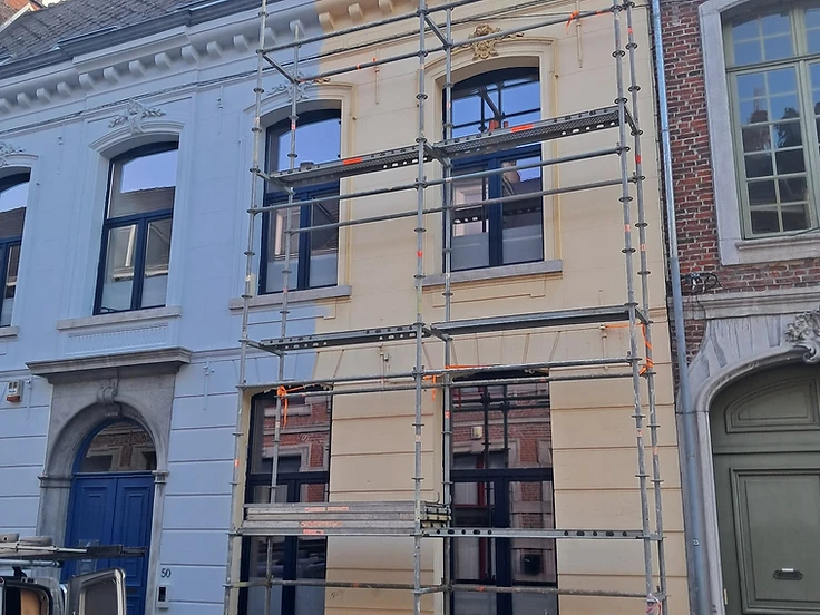 Échafaudage sur façade de maison de ville, moitié repeinte en bleu clair et moitié en jaune