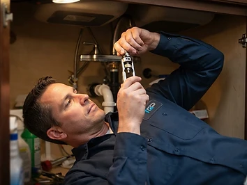Plumber repairing a kitchen faucet cartridge under the sink