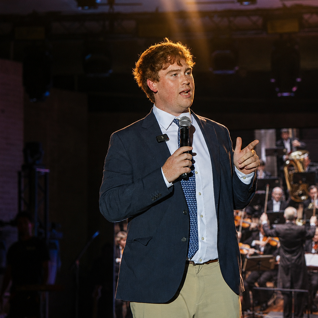 Dan Swords addressing the audience on stage with the orchestra