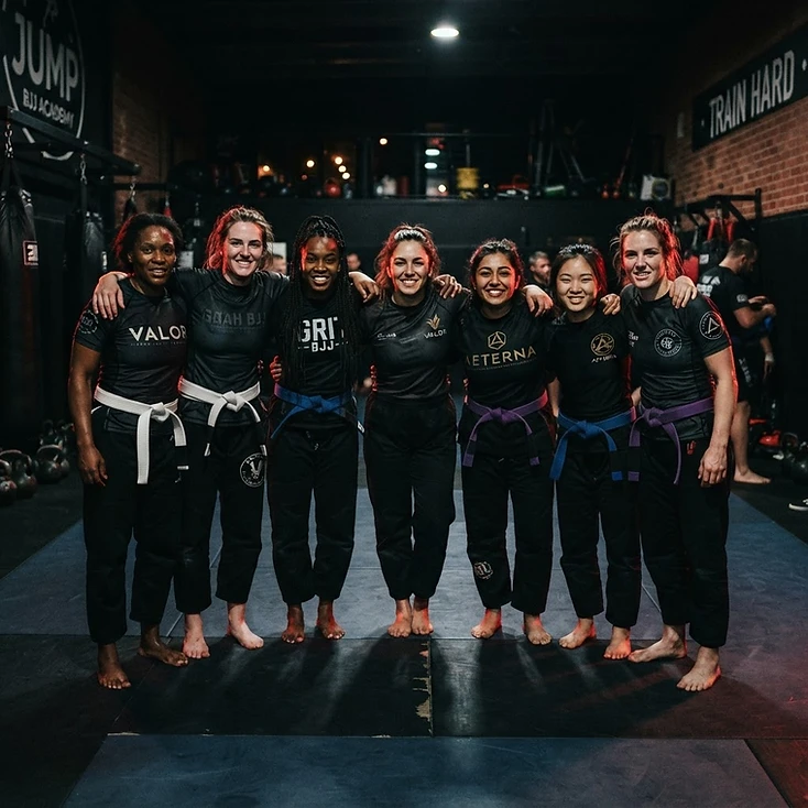 A group of female BJJ grapplers standing together in solidarity on the mat