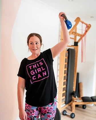 Member pressing a kettlebell overhead in a This Girl Can t-shirt