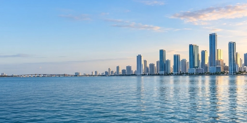 Miami waterfront with expansive blue morning sky, sunlit skyline to the right, and rippling harbor-blue water