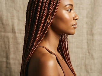 Profile portrait of waist-length copper-toned knotless braids with symmetrical parting