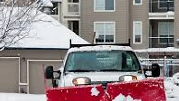 Pickup truck with a red snowplow clearing a residential driveway