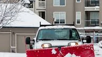 Snowplow truck clearing a residential driveway after snowfall