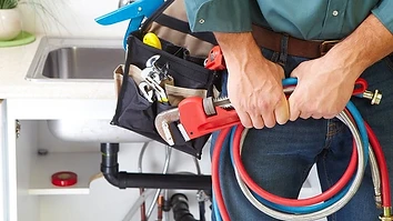 Plumber working under a kitchen sink with a pipe wrench