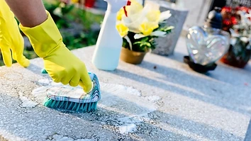 Hands in yellow gloves scrubbing a granite gravestone clean