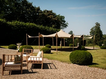 Tente stretch sable dressée sur un parterre de gravier avec fauteuils et topiaires