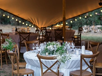Table ronde dressée avec composition florale sous une tente stretch éclairée au crépuscule