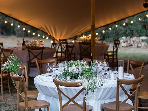 Table ronde dressée avec composition florale sous une tente stretch éclairée au crépuscule