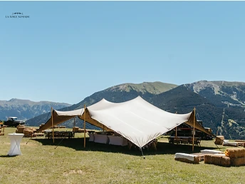 Tente stretch blanche dressée sur un terrain en pente face à des montagnes
