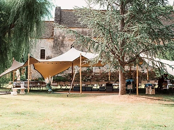 Tente stretch dressée dans un parc devant une maison en pierre avec banquet dressé