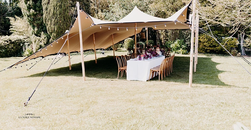 Tente stretch dressée dans un jardin, table dressée et guirlandes pour une réception privée