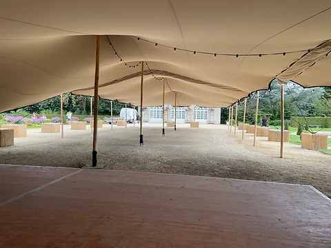 Tente stretch dressée sur un plancher face à une bâtisse en pierre