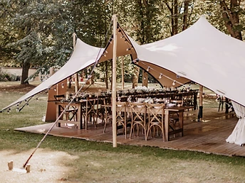 Tente stretch beige dressée sur un plancher dans un jardin arboré avec guirlandes