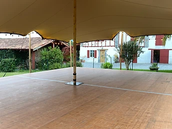 Sous une tente stretch, plancher bois donnant sur un jardin et une maison à pans de bois